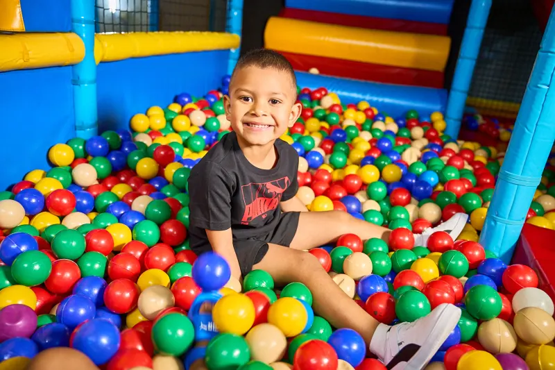 smiling young boy sitting in colorful ball pit at indoor play area