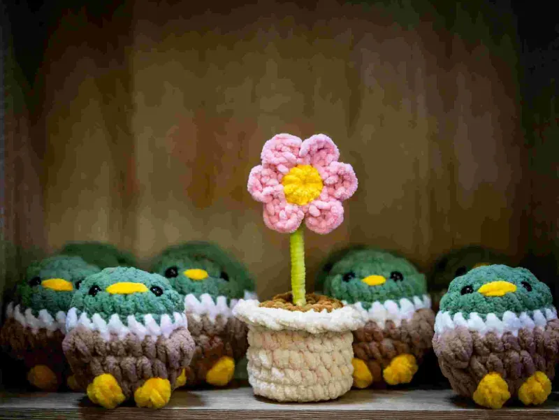 crocheted pink flower in a pot surrounded by small bird amigurumi toys on a shelf